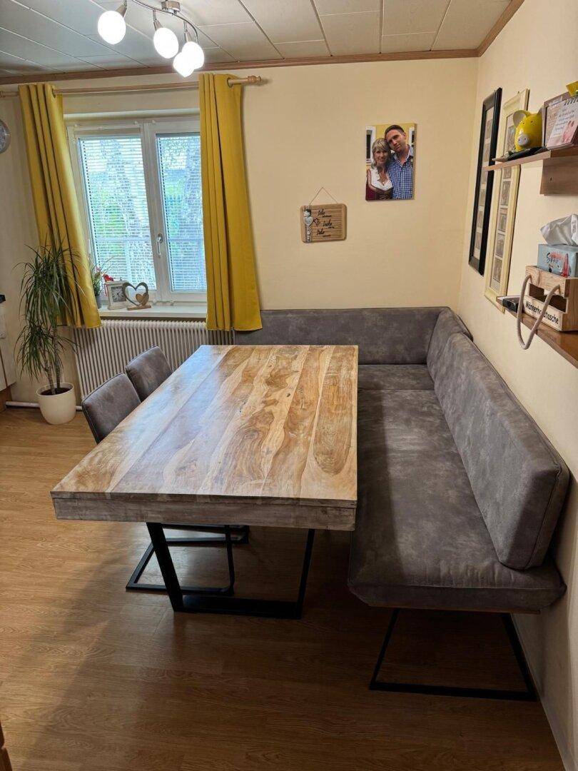 Essbereich mit großem Holztisch, Eckbank und gelben Vorhängen am Fenster.