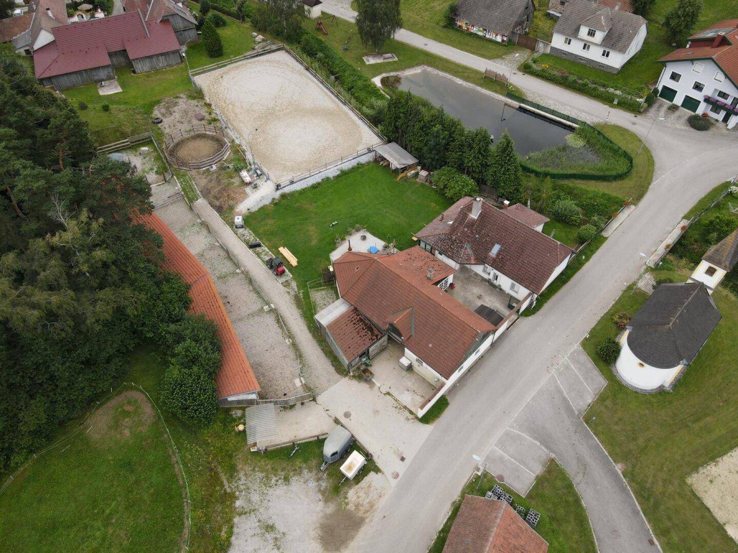 Weitläufige Luftaufnahme des Anwesens mit Reitplatz, Teich und angrenzendem Dorf.