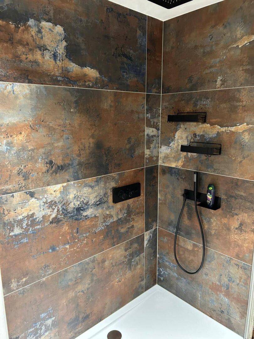Moderne Dusche mit großformatigen Fliesen in Rostoptik und schwarzen Armaturen.