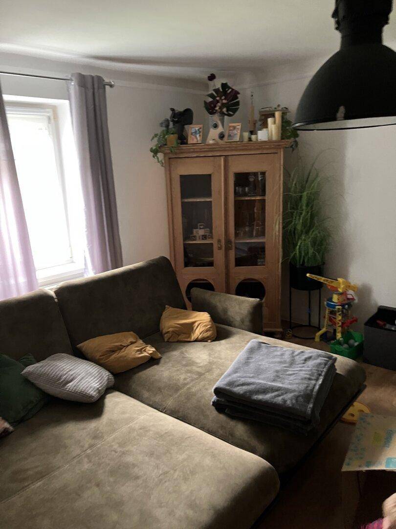Gemütliches Wohnzimmer mit großem Ecksofa, Holzschrank und Fenster.