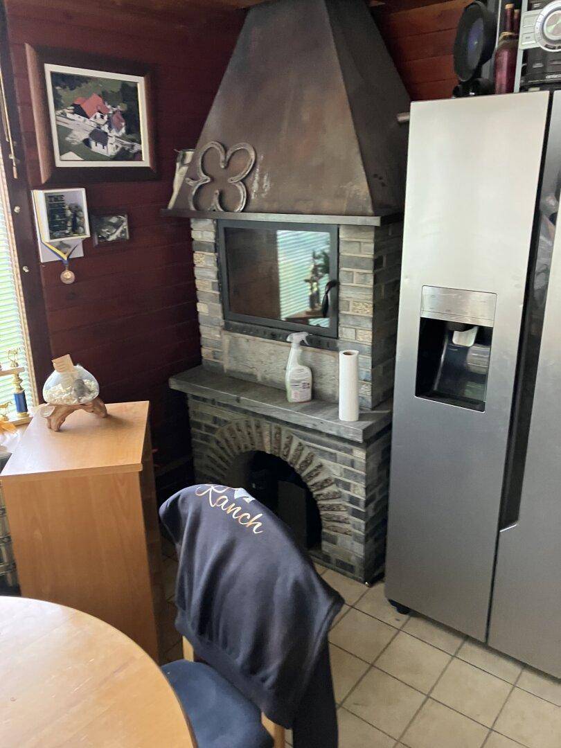 Rustikale Küche mit Kamin, großem Kühlschrank und Holzvertäfelung an den Wänden.