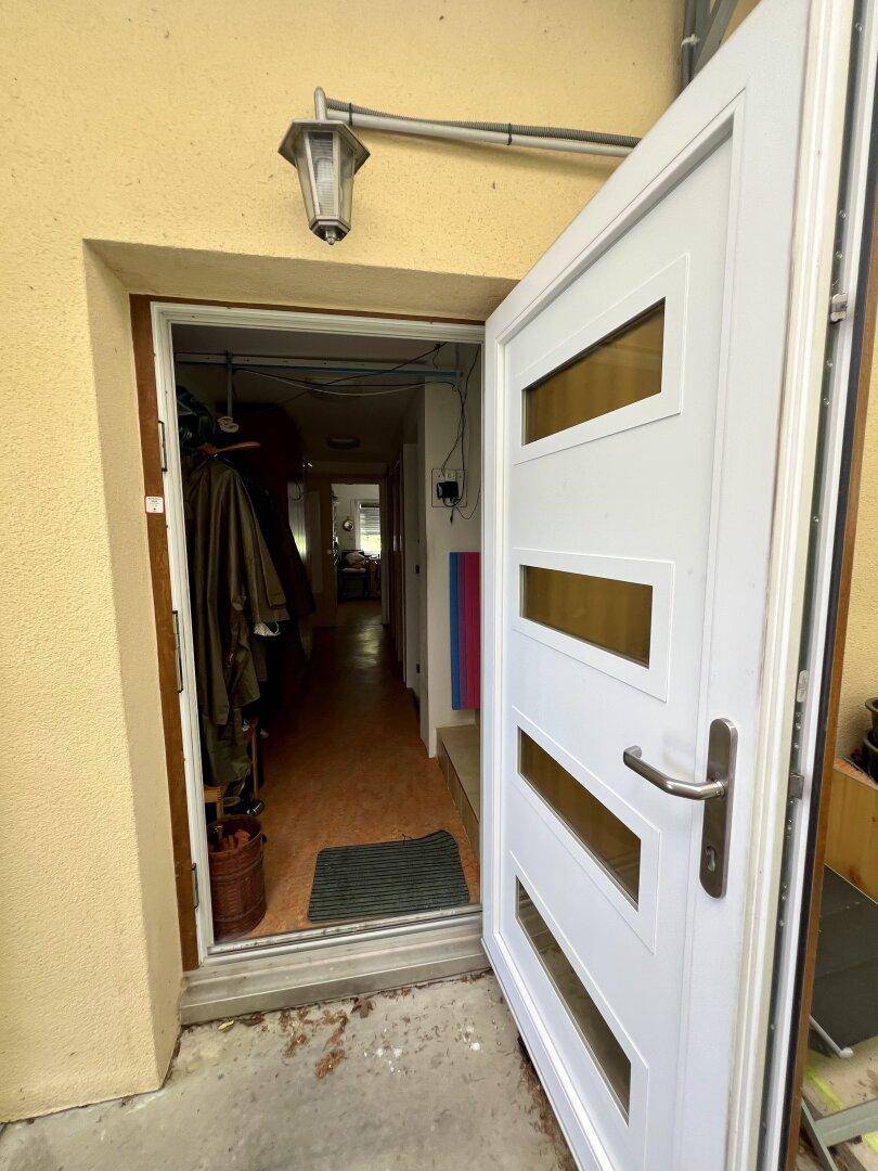 Offene weiße Eingangstür führt in einen schmalen Flur mit hellem Boden und Garderobe.