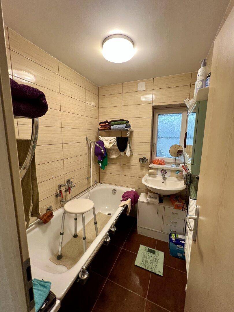Badezimmer mit beigefarbenen Fliesen, Badewanne, Waschbecken mit Spiegelschrank und Fenster.