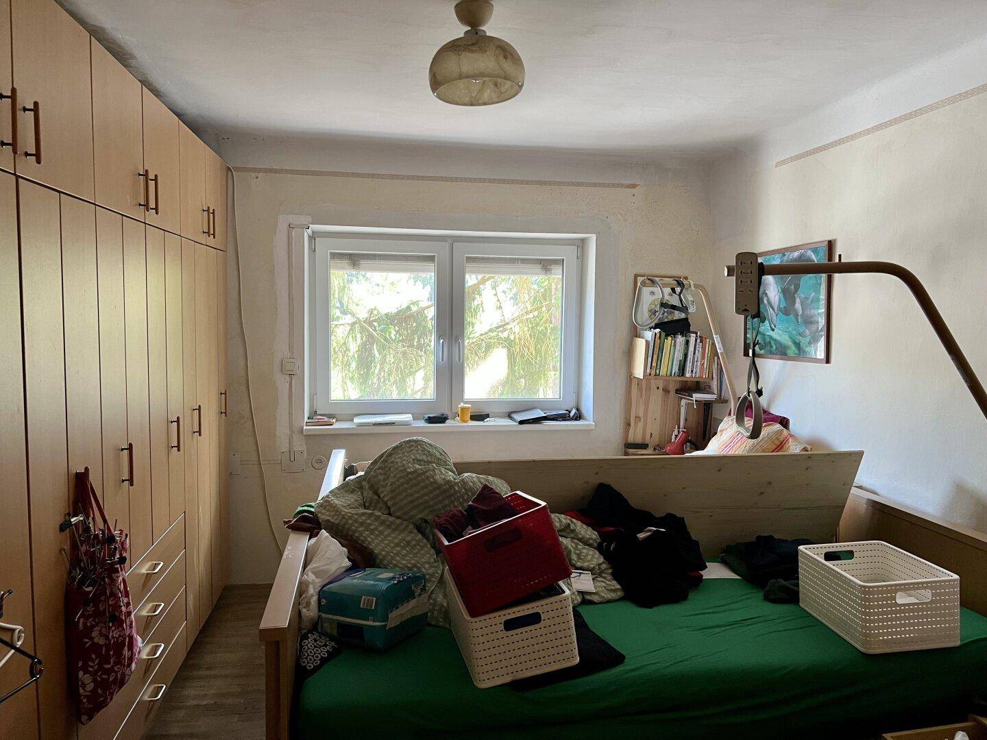 Schlafzimmer mit Bett, Holzschrank und Fenster, einfach und funktional eingerichtet.