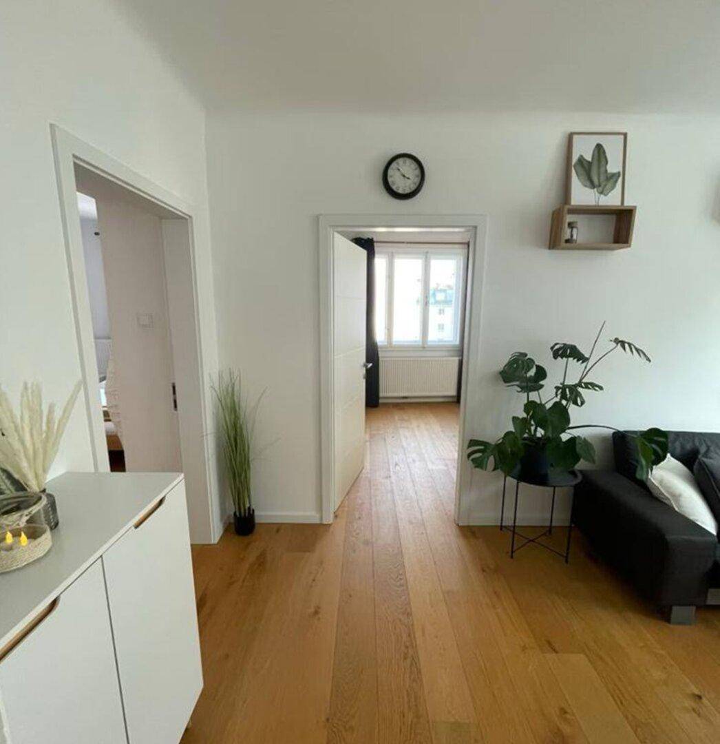 Heller Flur mit Holzboden, weißer Kommode und Blick in angrenzende Räume.