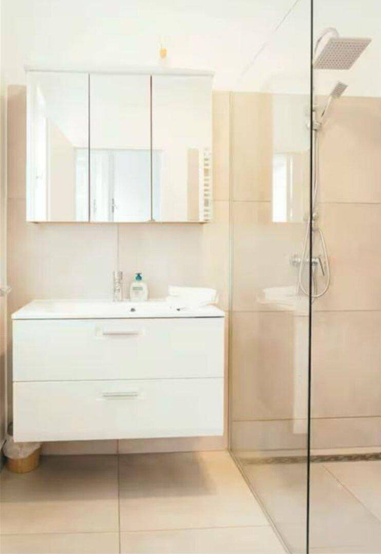 Modernes Badezimmer mit weißem Waschtisch, Spiegelschrank und ebenerdiger Dusche.