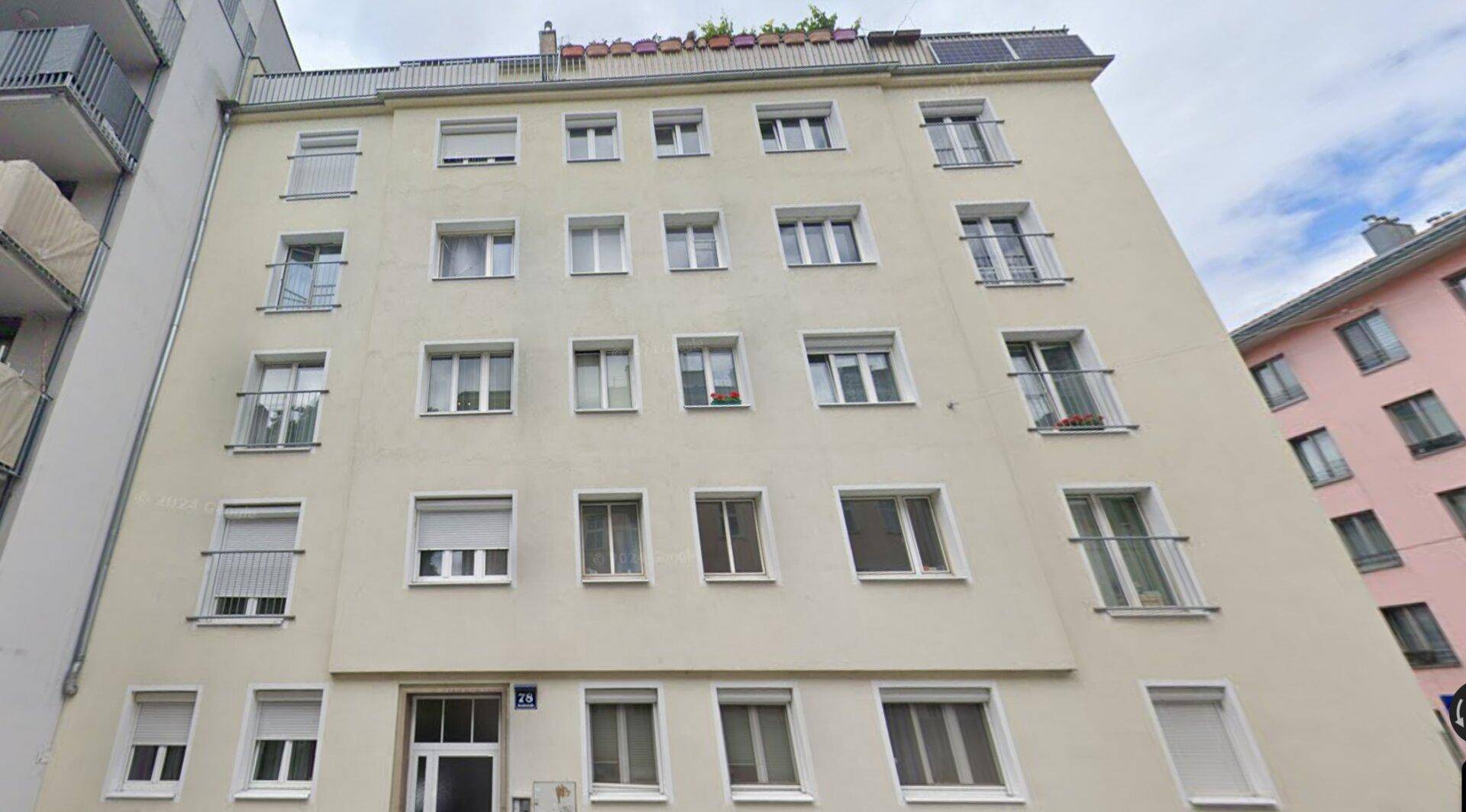 Mehrfamilienhaus mit heller Fassade, vielen Fenstern und kleinen Balkonen.