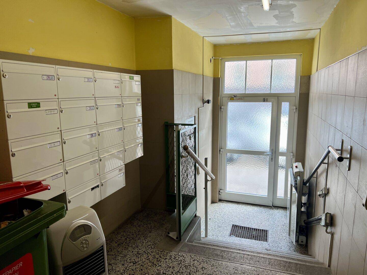 Eingangsbereich eines Mehrfamilienhauses mit Briefkästen, Rampe und Terrazzoboden.