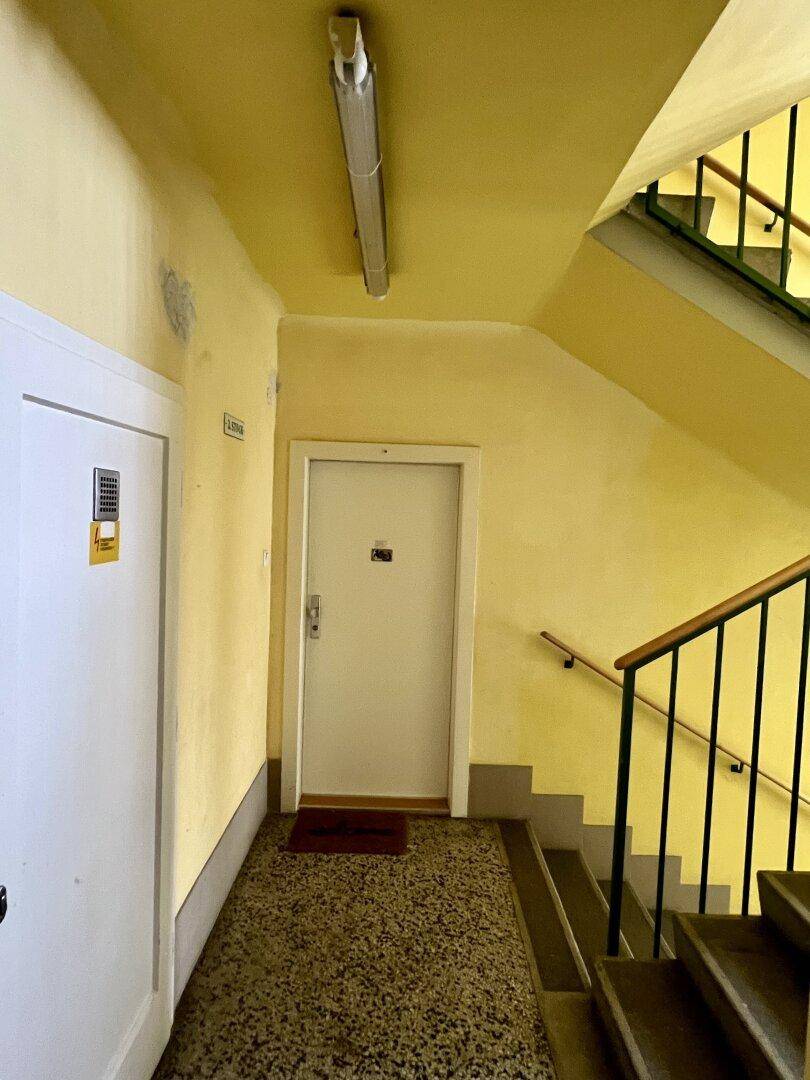 Heller Treppenabsatz mit gelben Wänden, Terrazzoboden und Zugang zu Wohnungen.