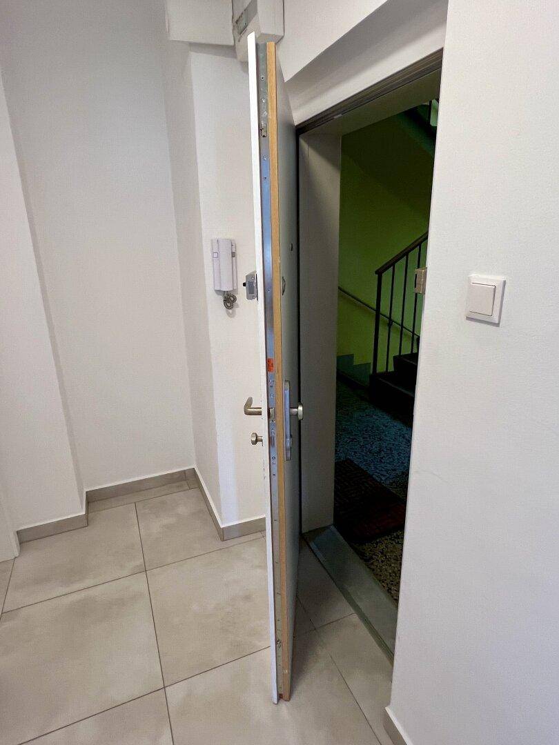 Eingangsbereich mit Fliesenboden und offener Wohnungstür, die zum Treppenhaus führt.