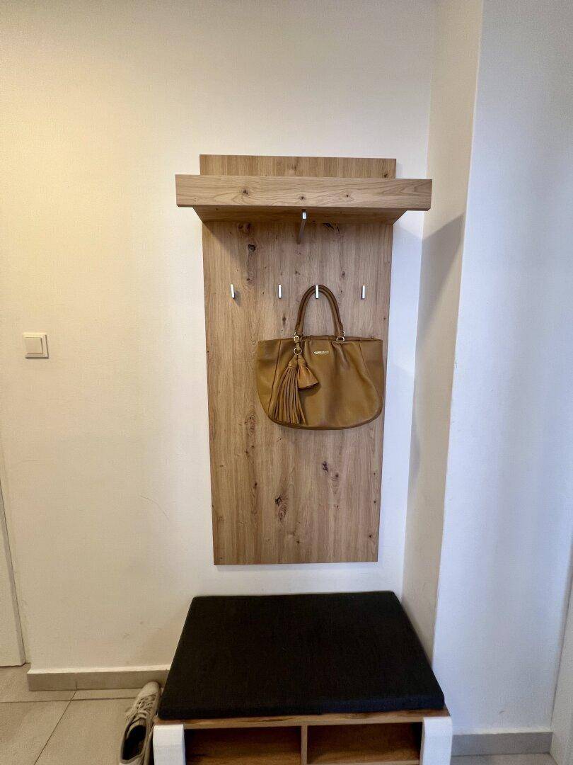 Heller Flur mit Holzkleiderhaken, Sitzbank und Ablagefläche für Schuhe.