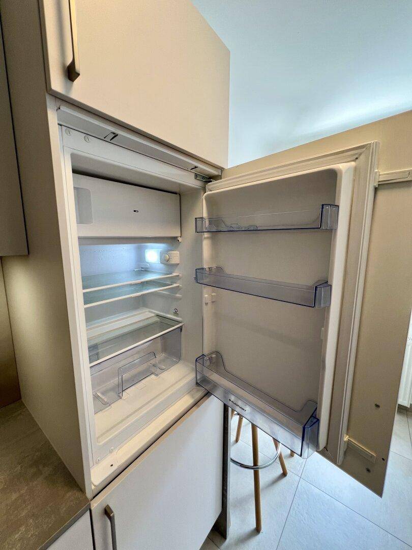 Integrierter Kühlschrank in einer modernen Küche mit hellgrauen Schränken und Fliesenboden.