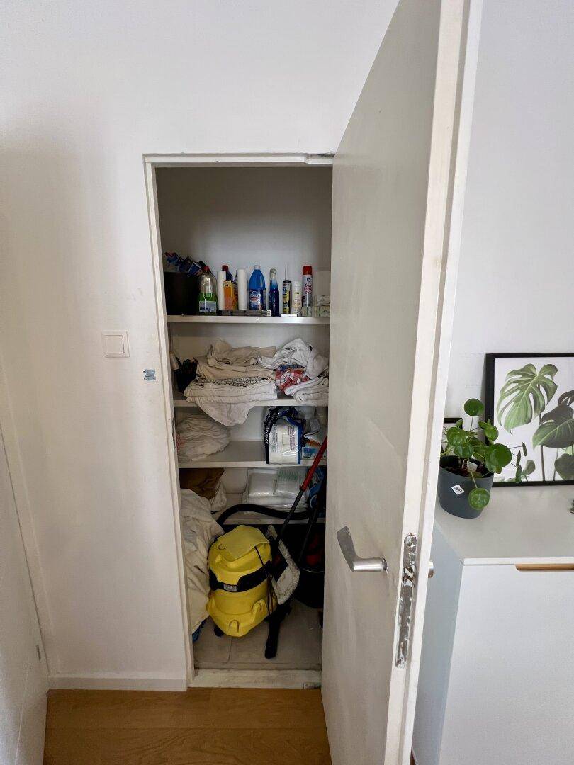 Offener Abstellraum mit Regalen, Reinigungsutensilien und Staubsauger.