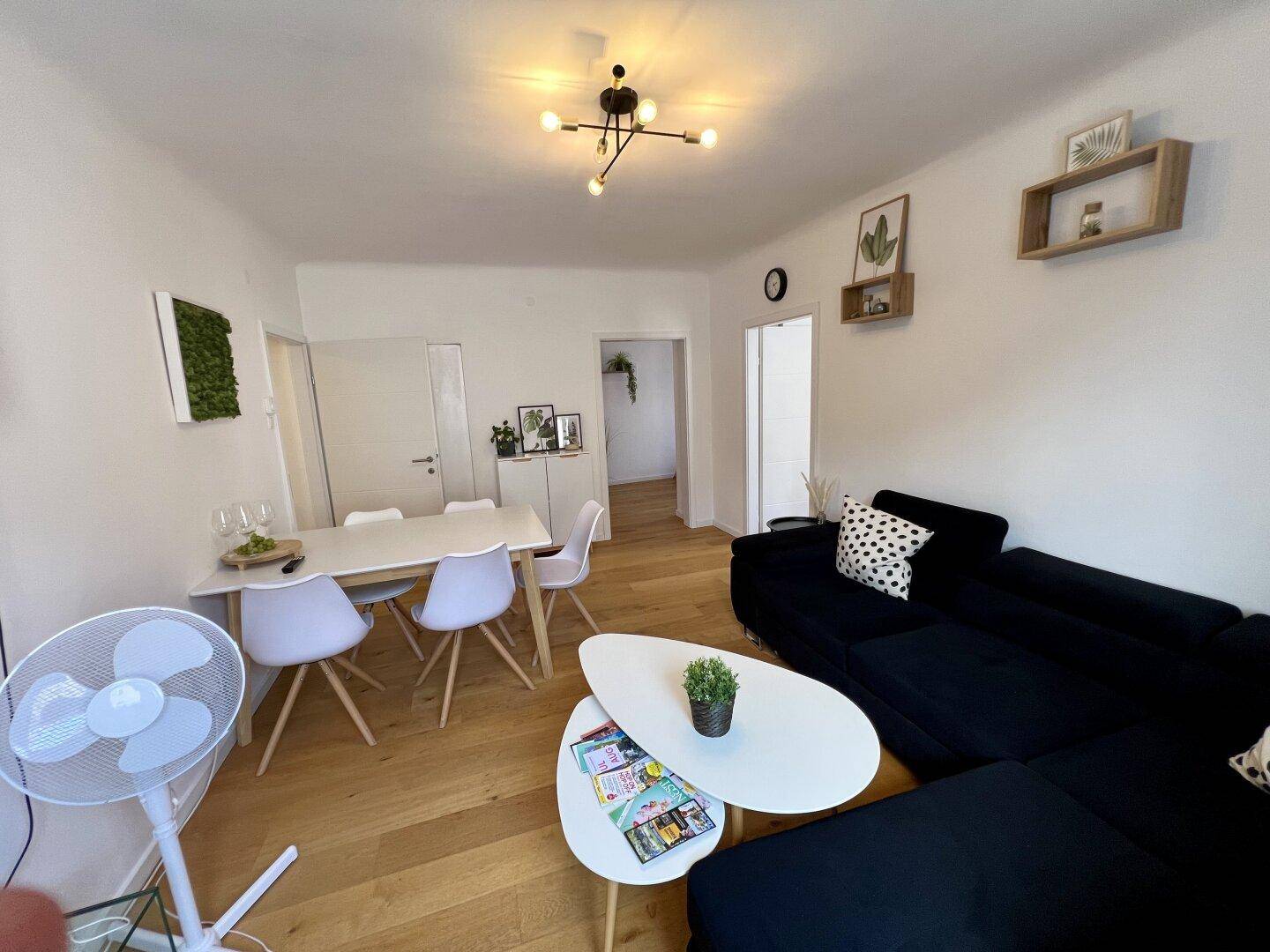 Geräumiger Wohn-Essbereich mit Holzboden, dunklem Sofa und modernem Esstisch für vier Personen.
