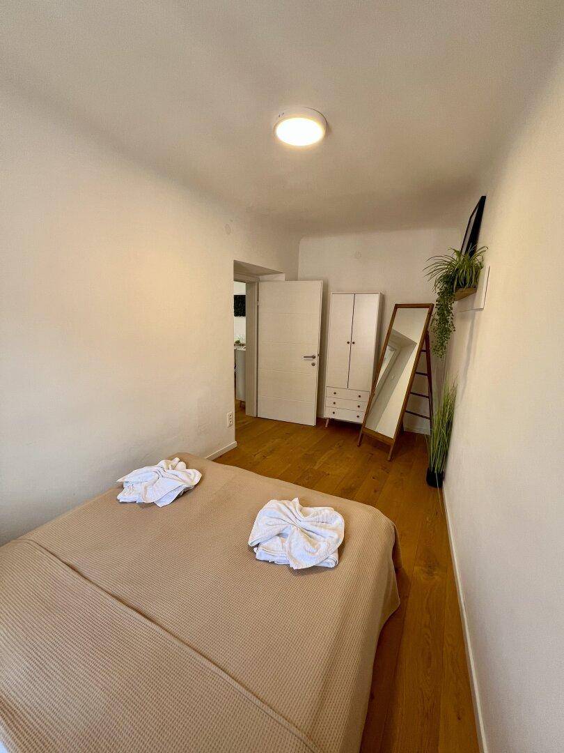 Schlafzimmer mit Holzboden, beigem Bett und einem Kleiderschrank mit Spiegel.