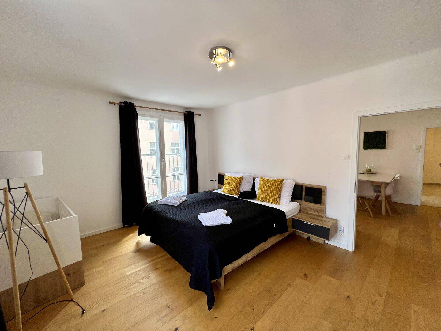 Schlafzimmer mit Holzboden, dunklem Bett und einem Fenster mit Blick nach draußen.