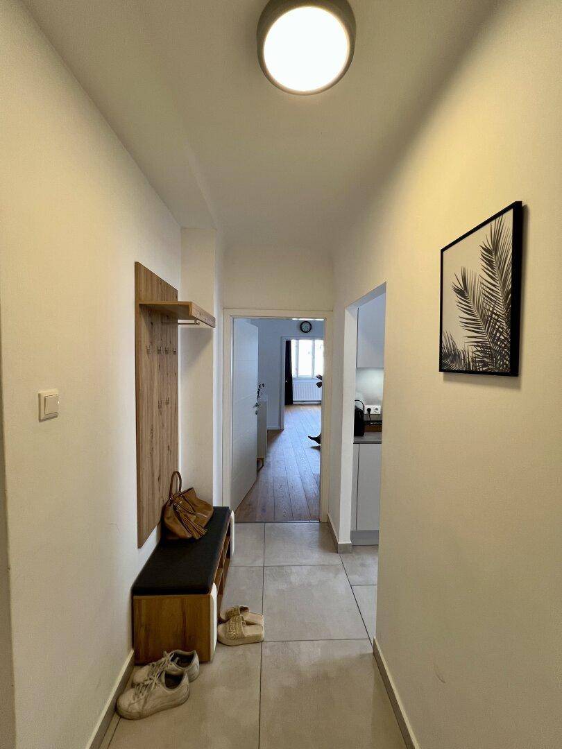 Heller Flur mit Fliesenboden, Garderobe und Blick in die angrenzende Küche.