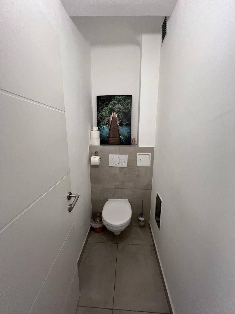 Modernes Gäste-WC mit Wand-WC, Fliesenboden und einem dekorativen Bild an der Wand.