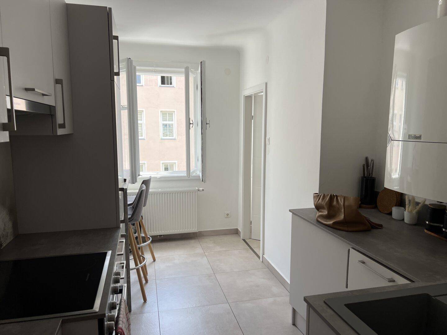 Helle Küche mit modernen Einbauschränken, Induktionskochfeld und Essbereich am Fenster.