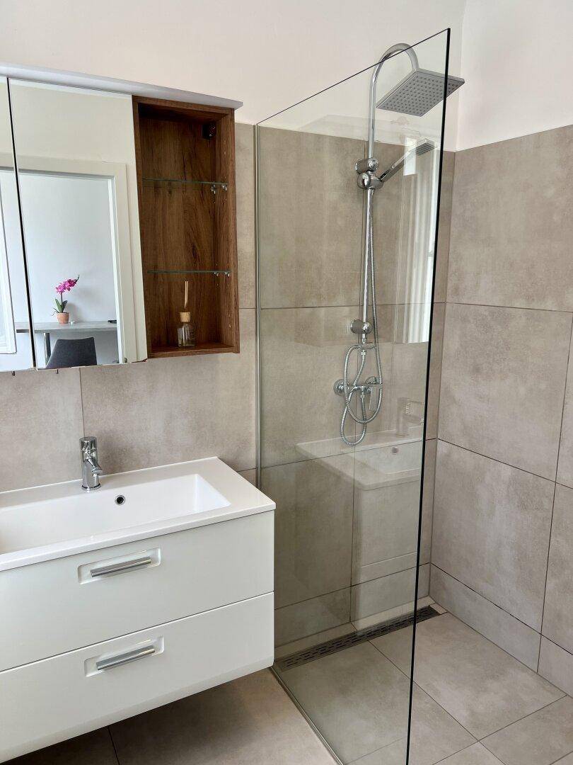Modernes Badezimmer mit ebenerdiger Dusche, Waschbecken und Spiegelschrank.