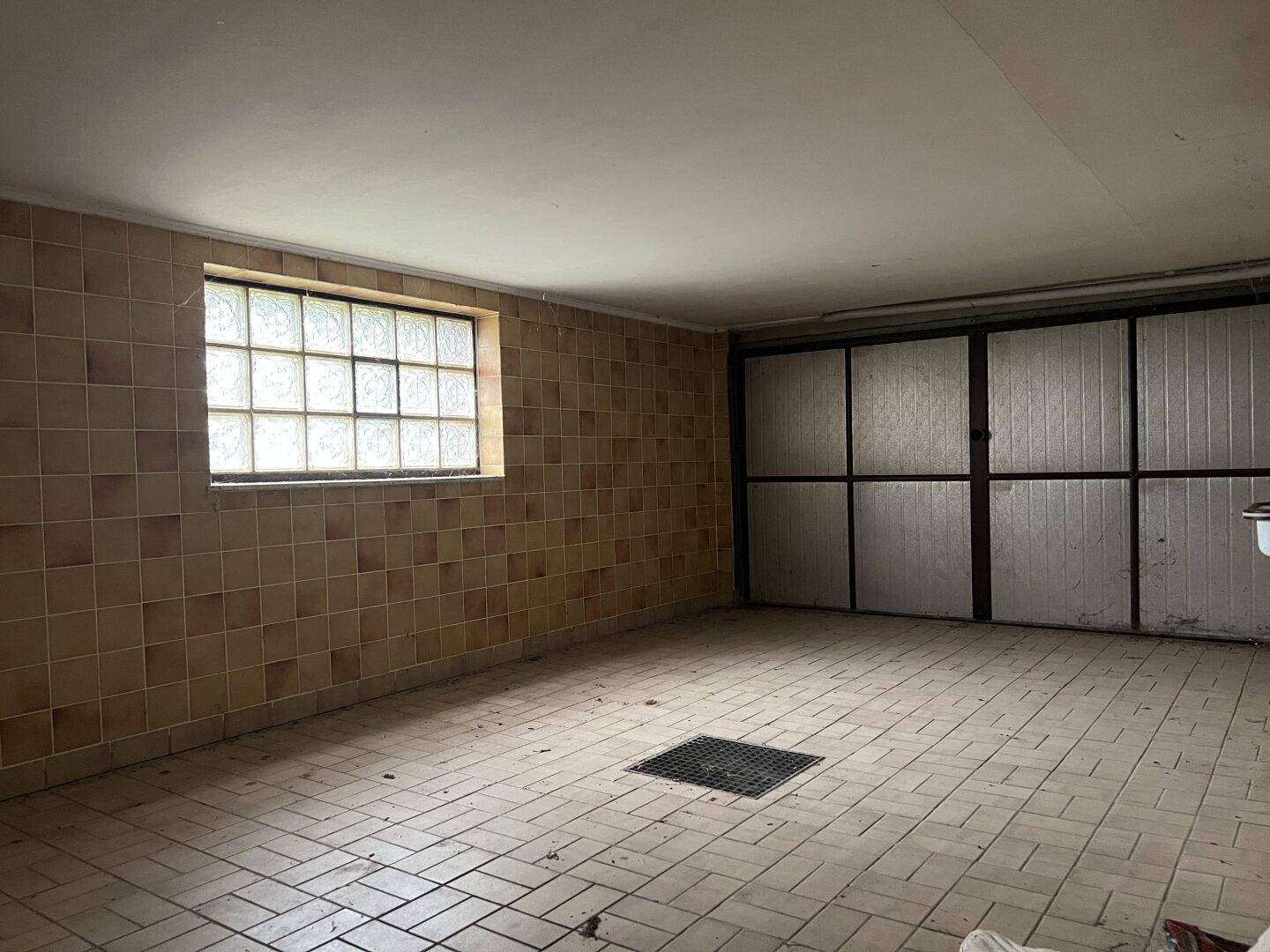 Geräumige Garage mit Fliesenboden, gefliesten Wänden und einem Fenster aus Glasbausteinen.