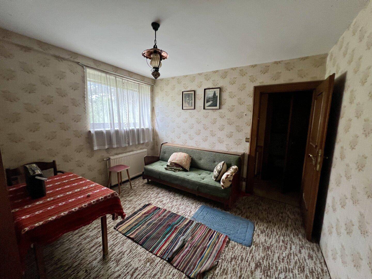 Wohnzimmer im Vintage-Stil mit gemusterter Tapete, Sofa und einem kleinen Esstisch.