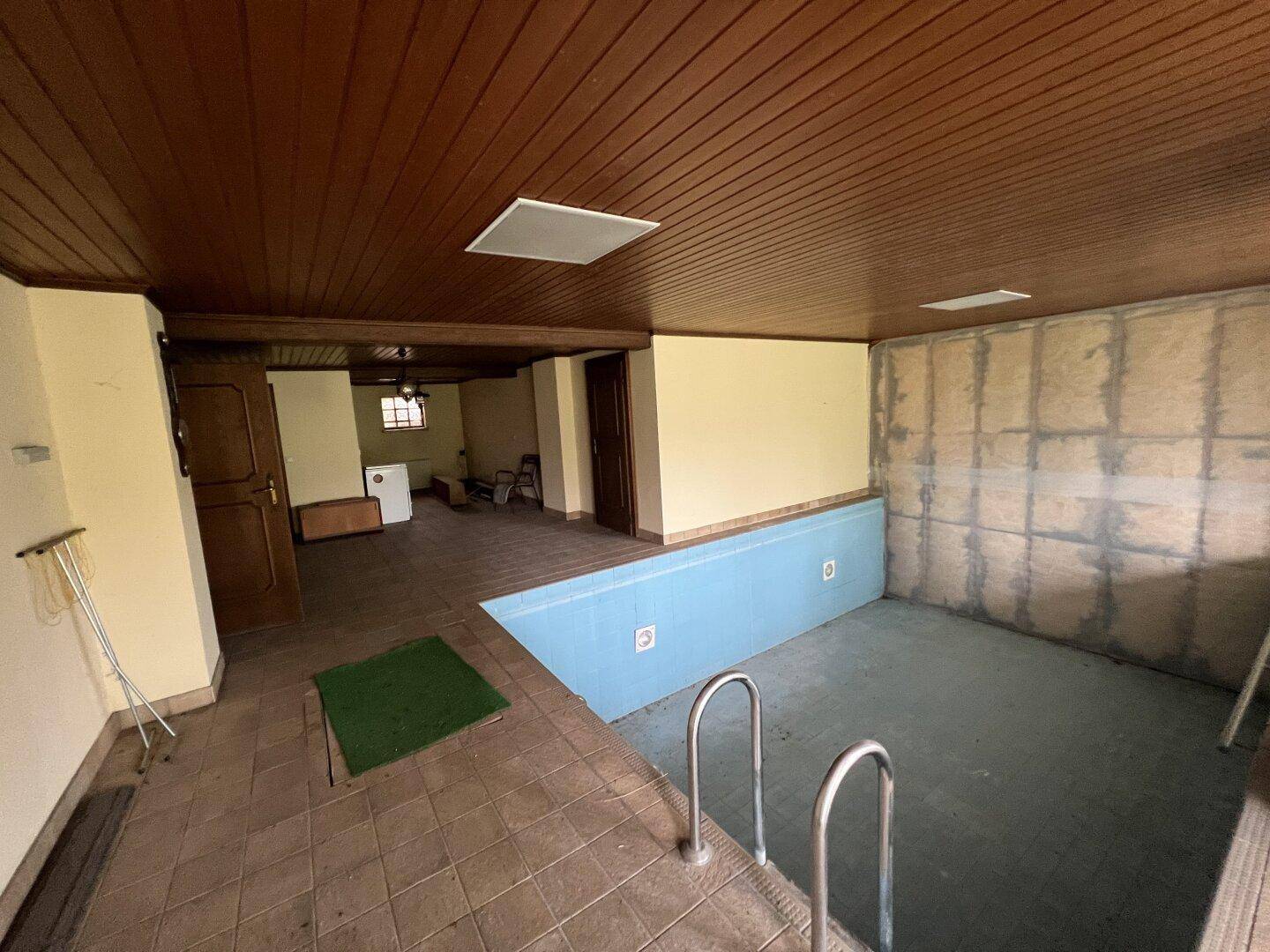 Innenpoolbereich mit Fliesenboden und Holzdecke, bereit zur Renovierung.