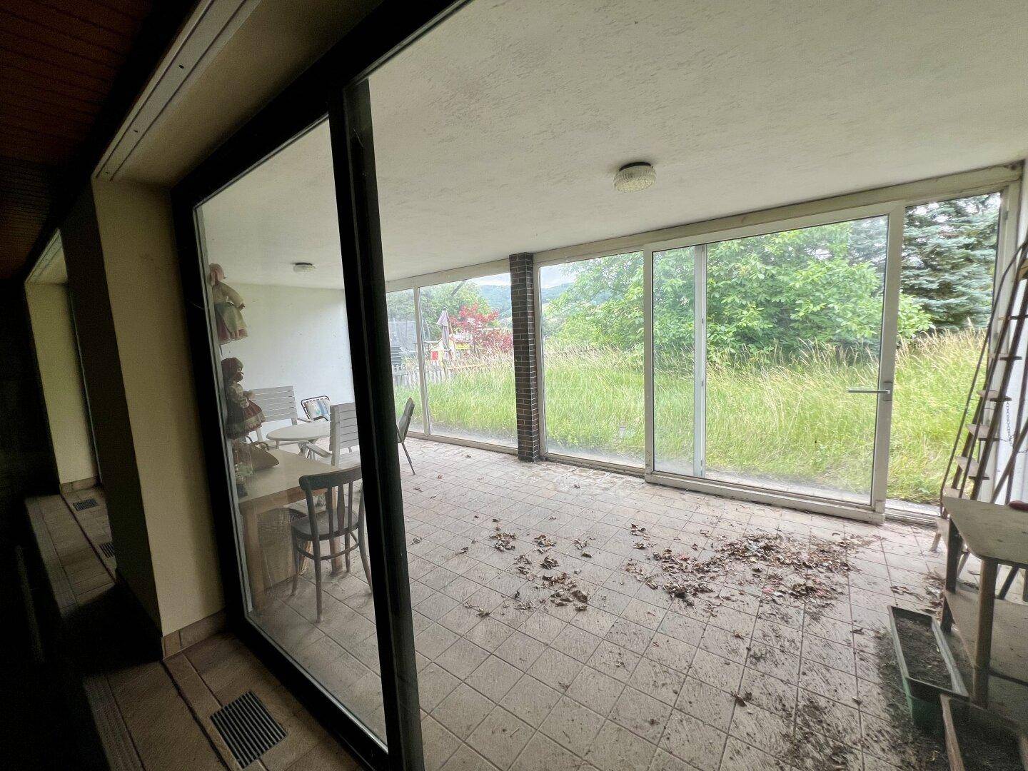 Blick vom Innenpoolbereich auf die verglaste Terrasse und die grüne Umgebung.