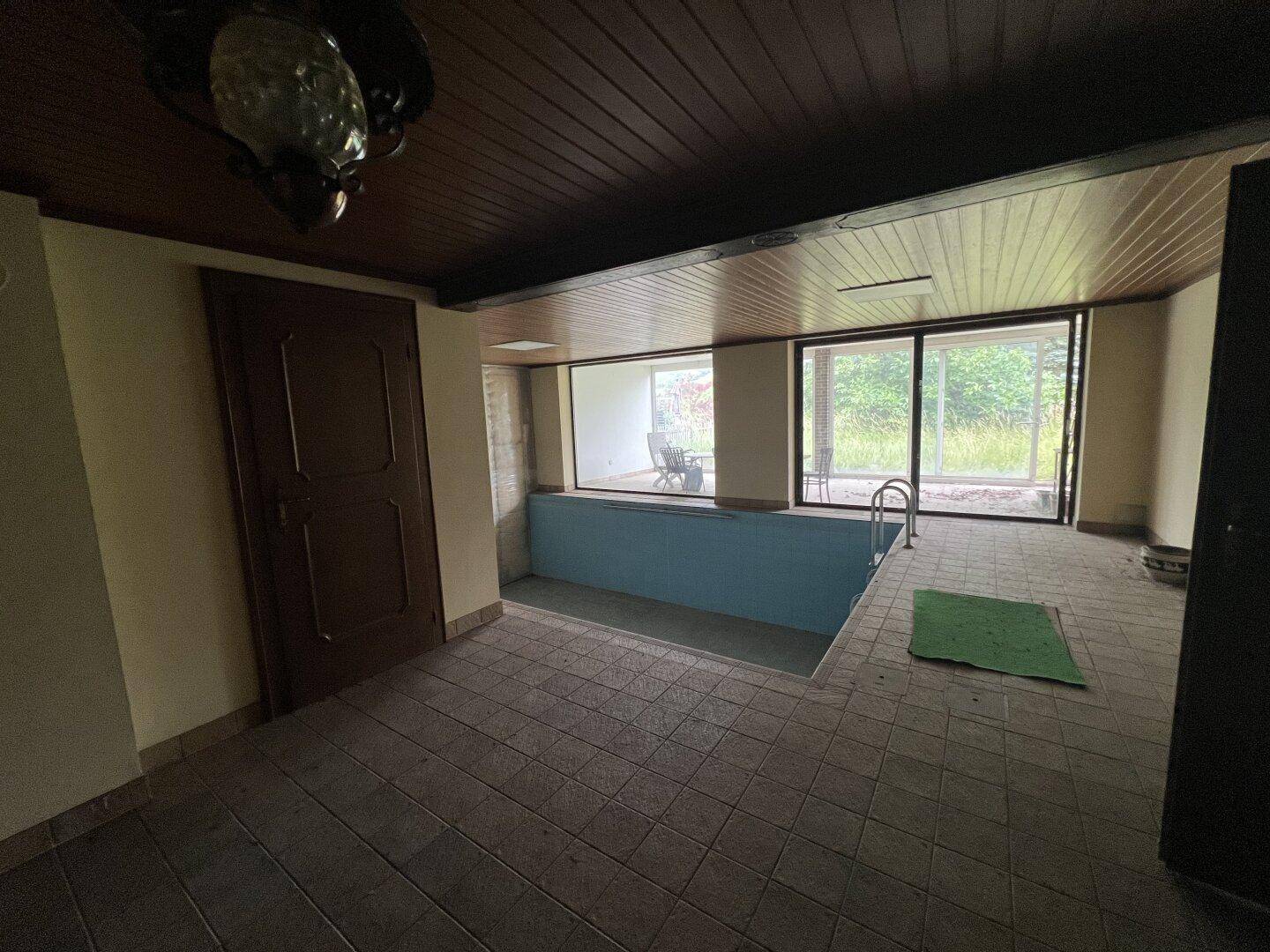 Innenpool mit Einstiegsleiter und gefliestem Boden, umgeben von großen Fenstern.