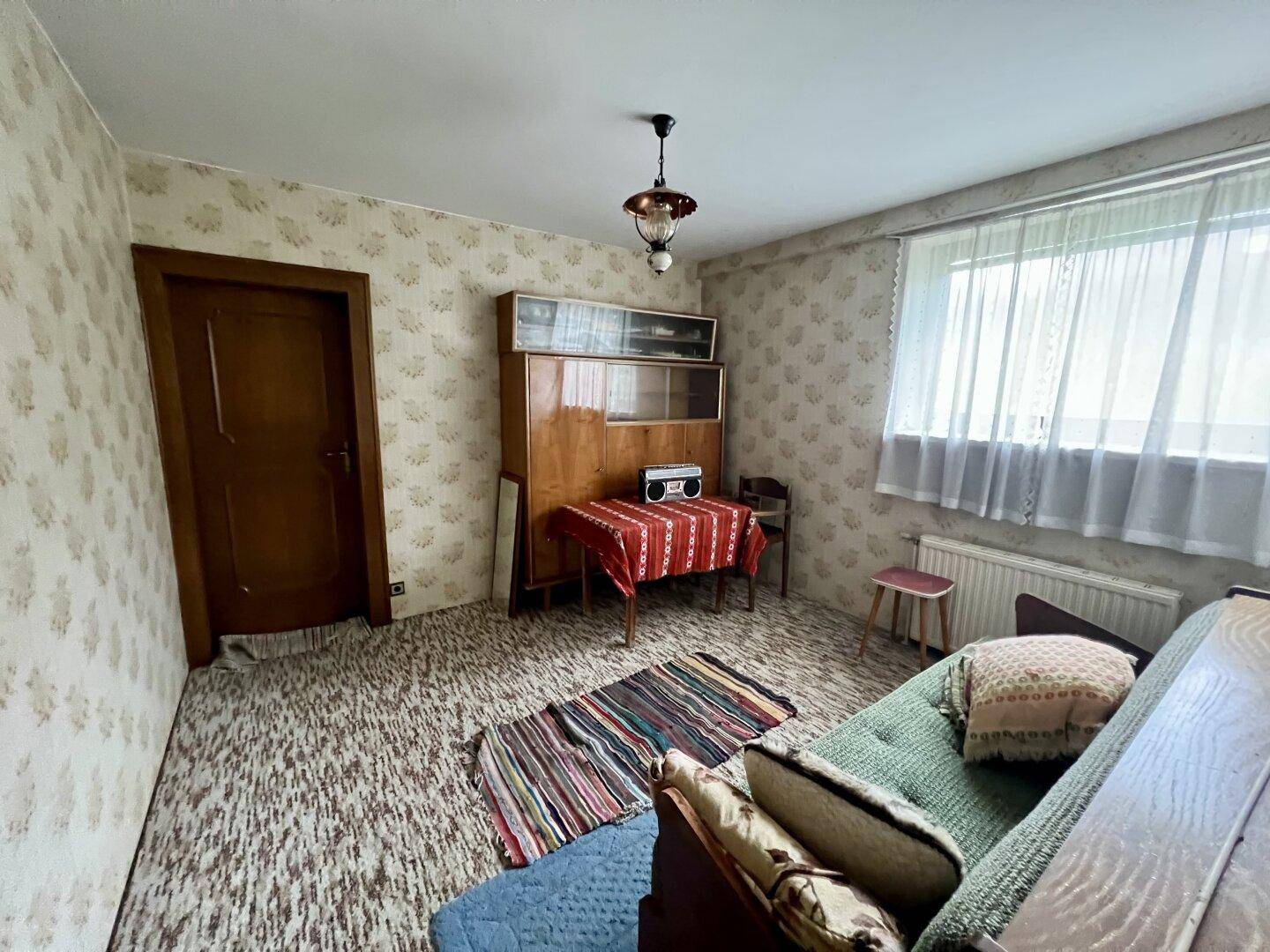 Wohnzimmer mit gemusterter Tapete, Sofa und einem klassischen Holzschrank.