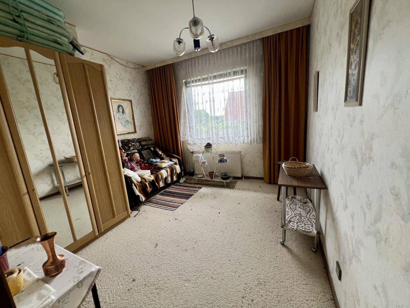 Schlafzimmer mit gemusterter Tapete, Kleiderschrank und einem Fenster mit Vorhängen.