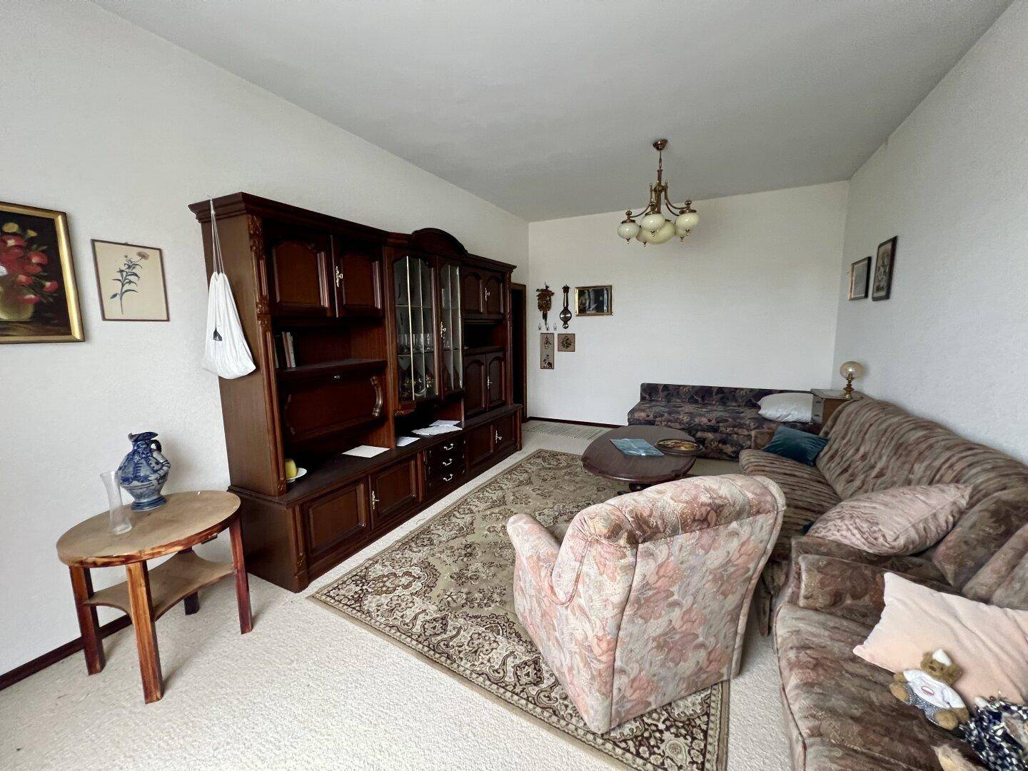 Geräumiges Wohnzimmer mit großem Holzschrank, Sofa und Teppichboden.