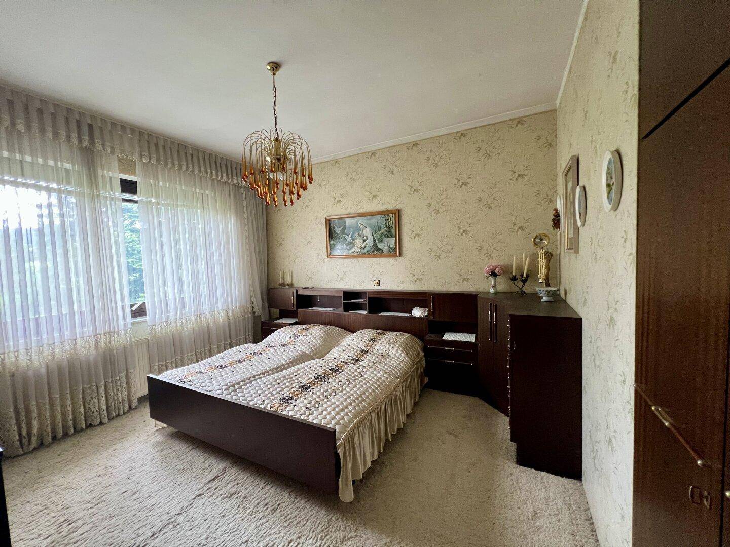 Geräumiges Schlafzimmer mit Teppichboden, großem Fenster und traditioneller Einrichtung.