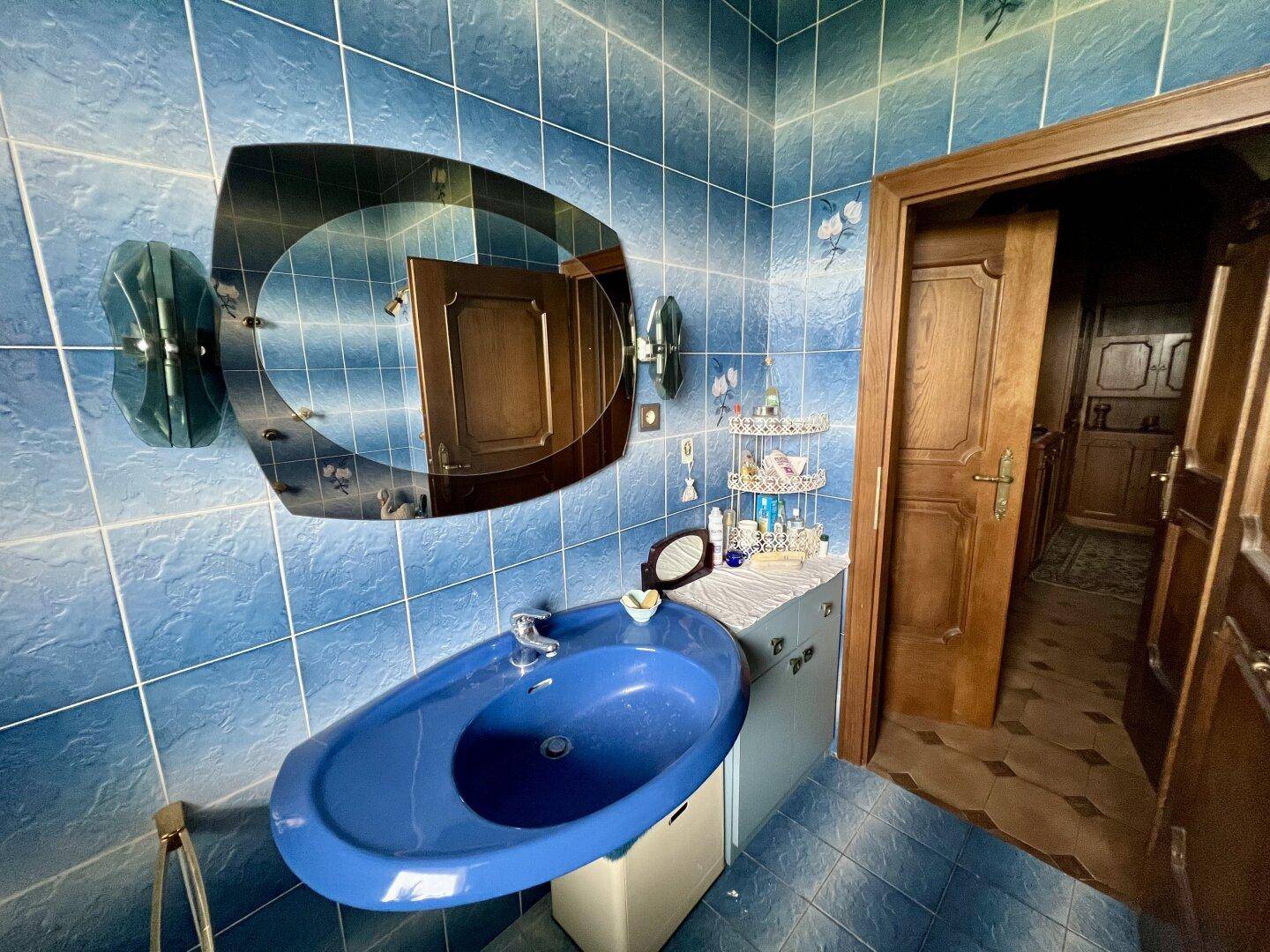 Badezimmer mit blauen Fliesen, einem blauen Waschbecken und einem großen, ovalen Spiegel.