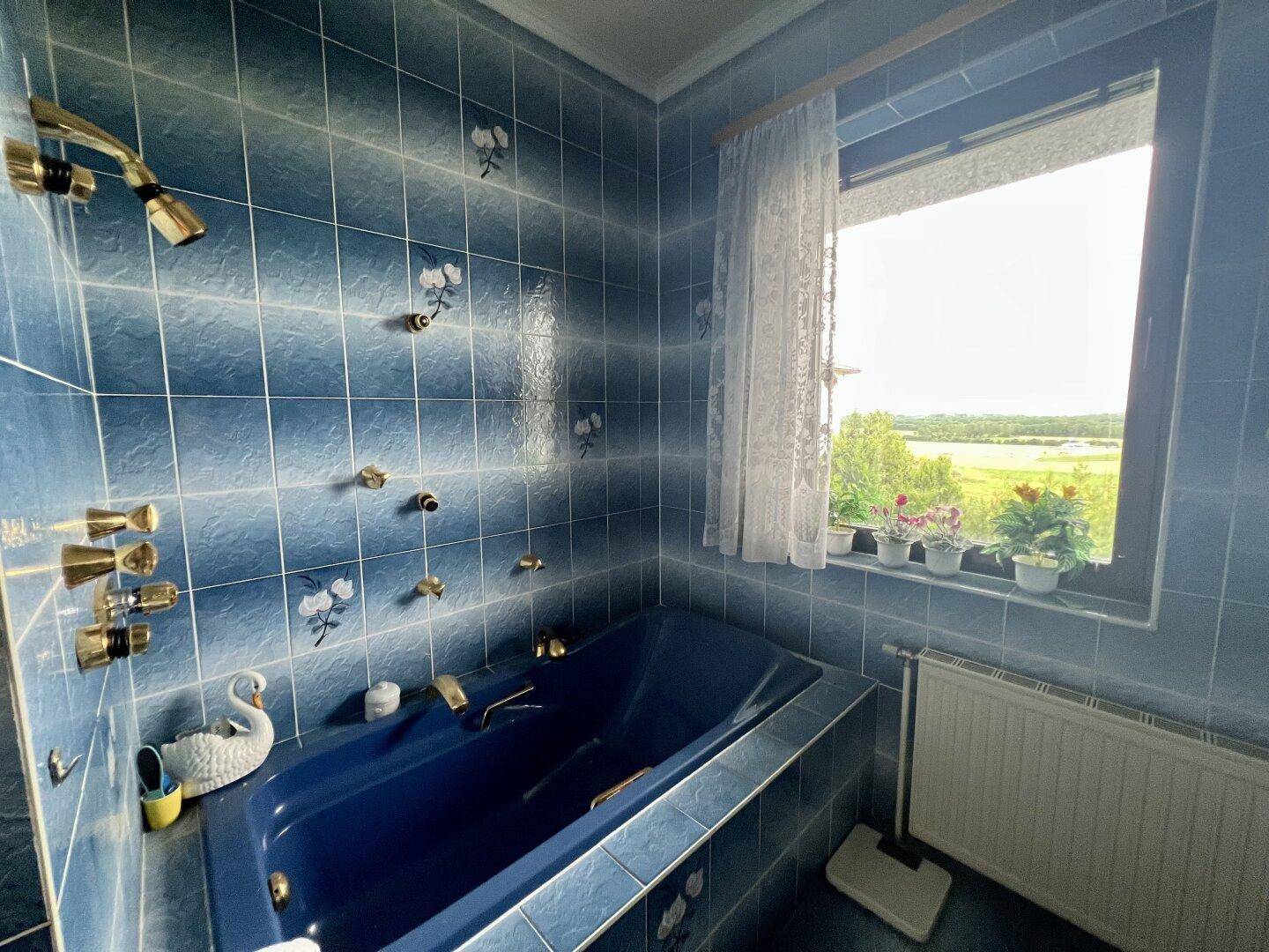 Badezimmer mit blauen Fliesen, Badewanne und Fenster mit Blick ins Grüne.