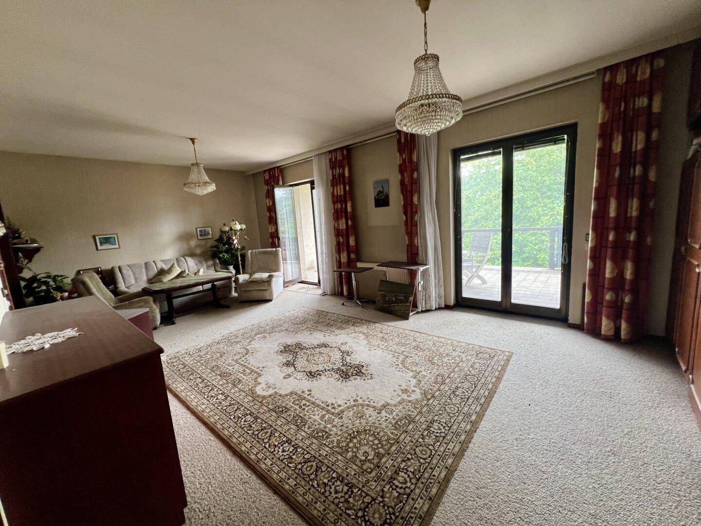 Großes Wohnzimmer mit Teppichboden, zwei Balkonzugängen und Kronleuchtern.