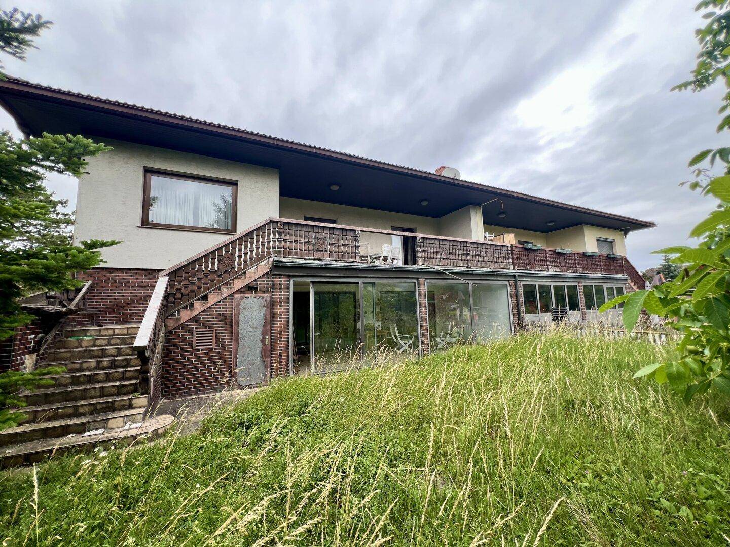 Ansicht des Hauses mit Außentreppe, Balkon und verglastem Wintergarten.
