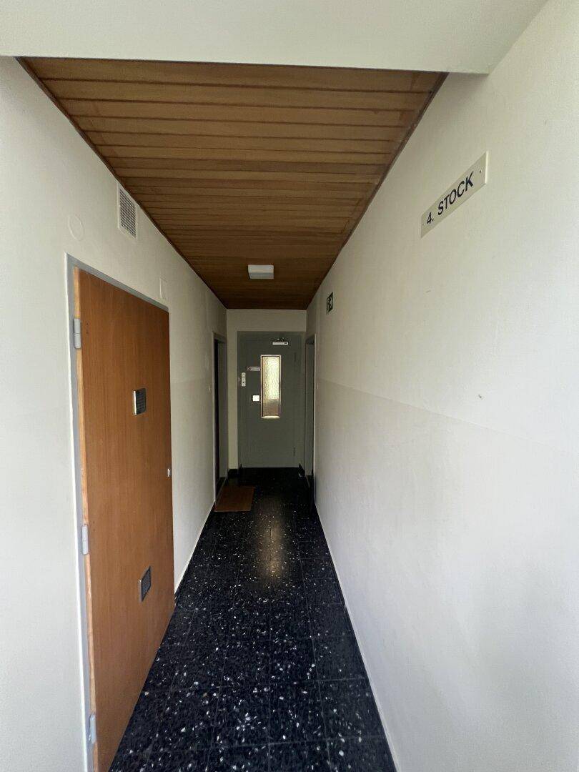 Langer Flur mit Holzdecke und dunklem Terrazzoboden, der zu weiteren Räumen führt.
