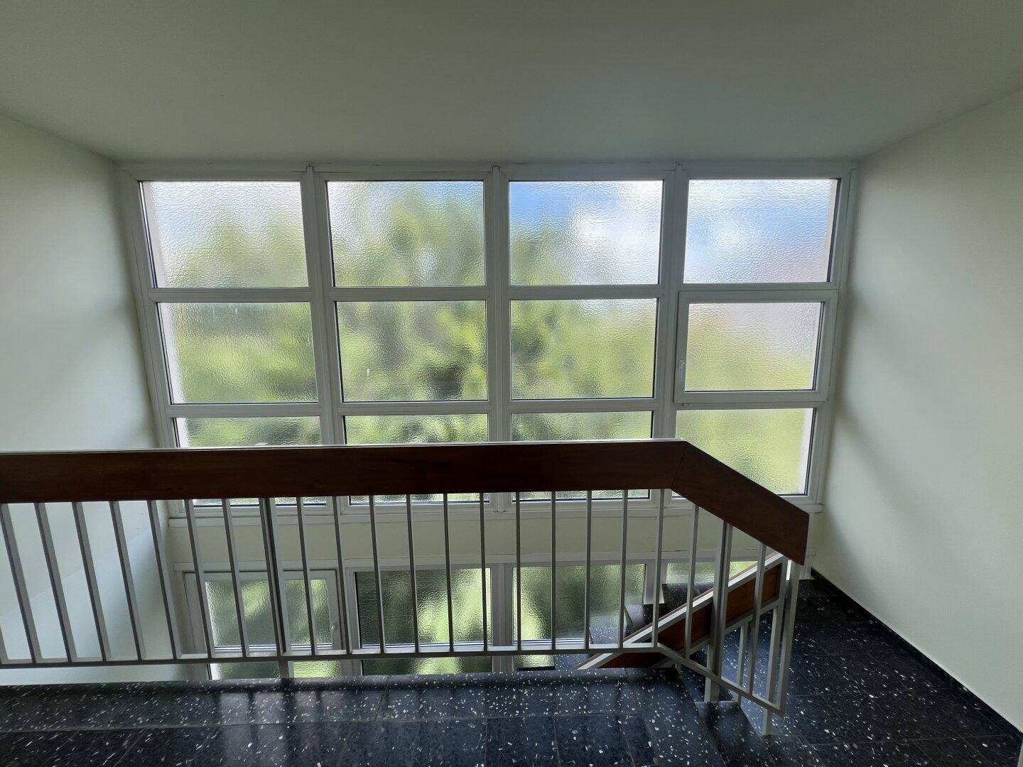 Blick von oben in ein Treppenhaus mit großen, undurchsichtigen Fenstern und viel Licht.