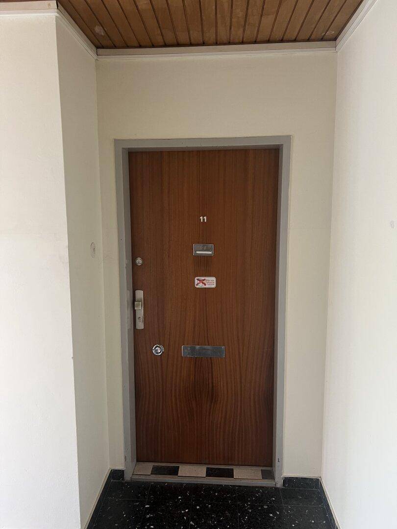 Eingangstür einer Wohnung mit der Nummer 11 und Holzverkleidung im Flurbereich.