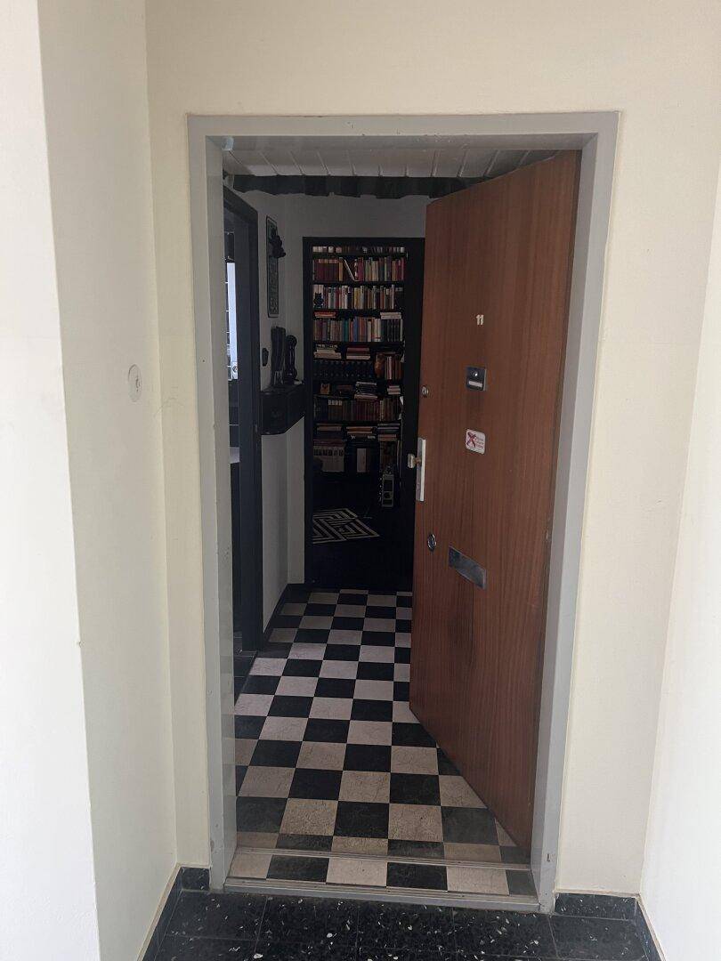 Geöffnete Wohnungstür, die den Blick auf einen schwarz-weiß karierten Fliesenboden freigibt.
