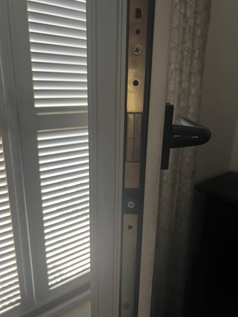 Nahaufnahme eines Türschlosses und Jalousien an einem Fenster, das Tageslicht hereinlässt.