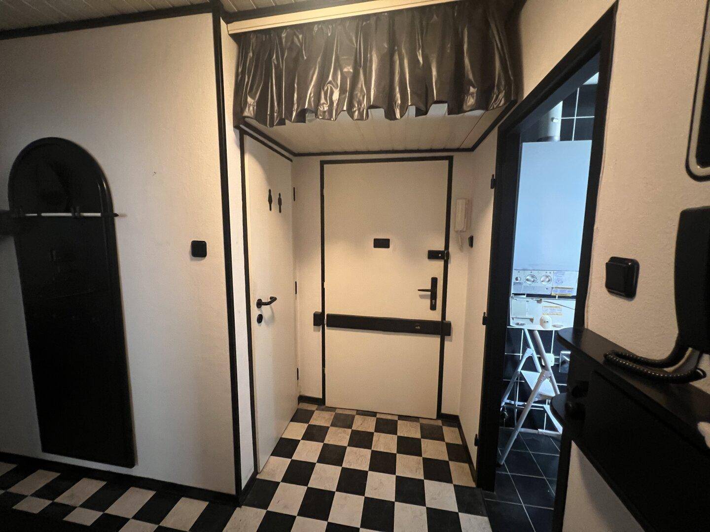 Eingangsbereich mit schwarz-weiß kariertem Boden und mehreren Türen, die zu den Räumen führen.
