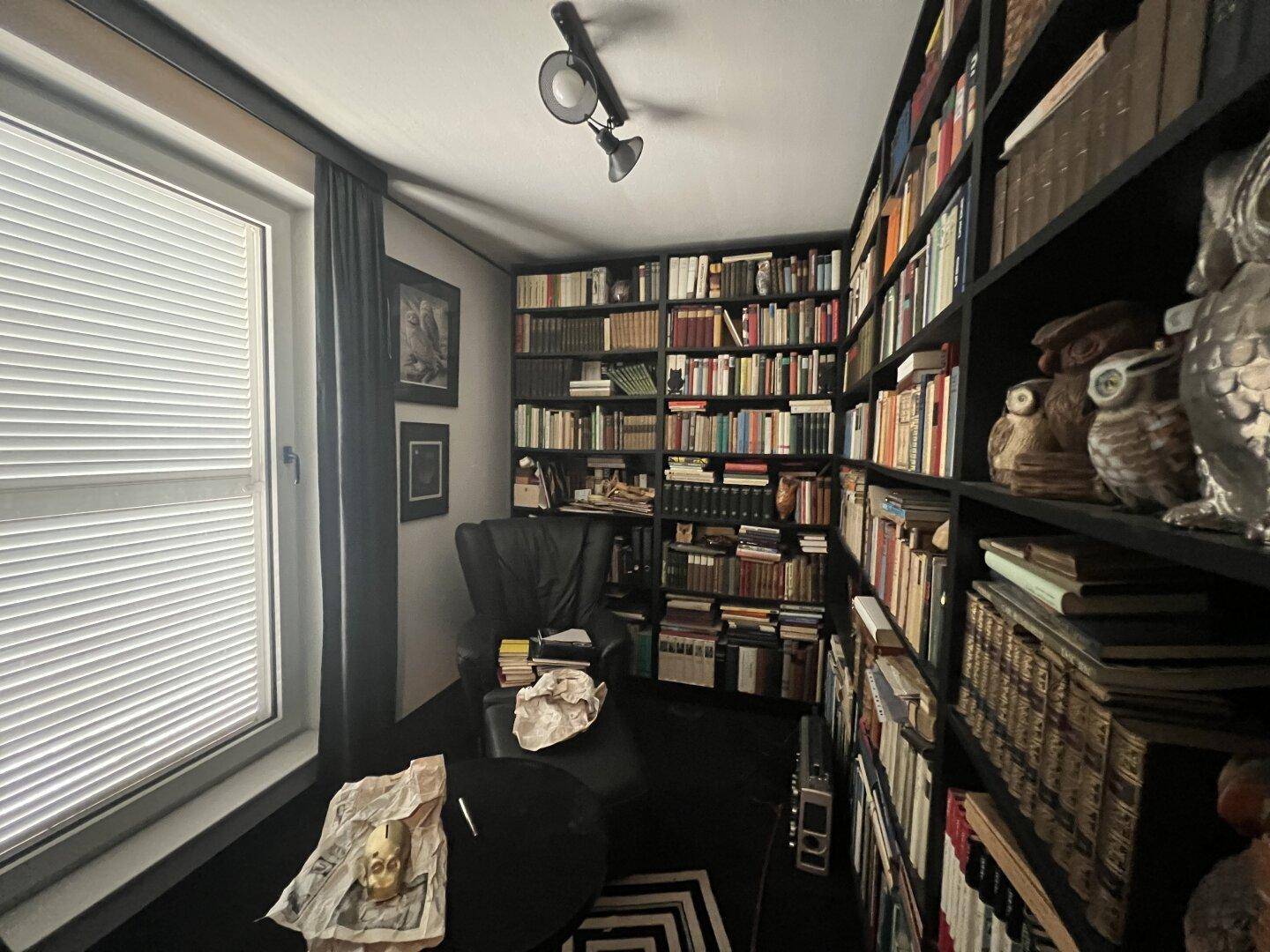 Arbeitszimmer mit raumhohen Bücherregalen, einem Schreibtisch und einem Fenster.