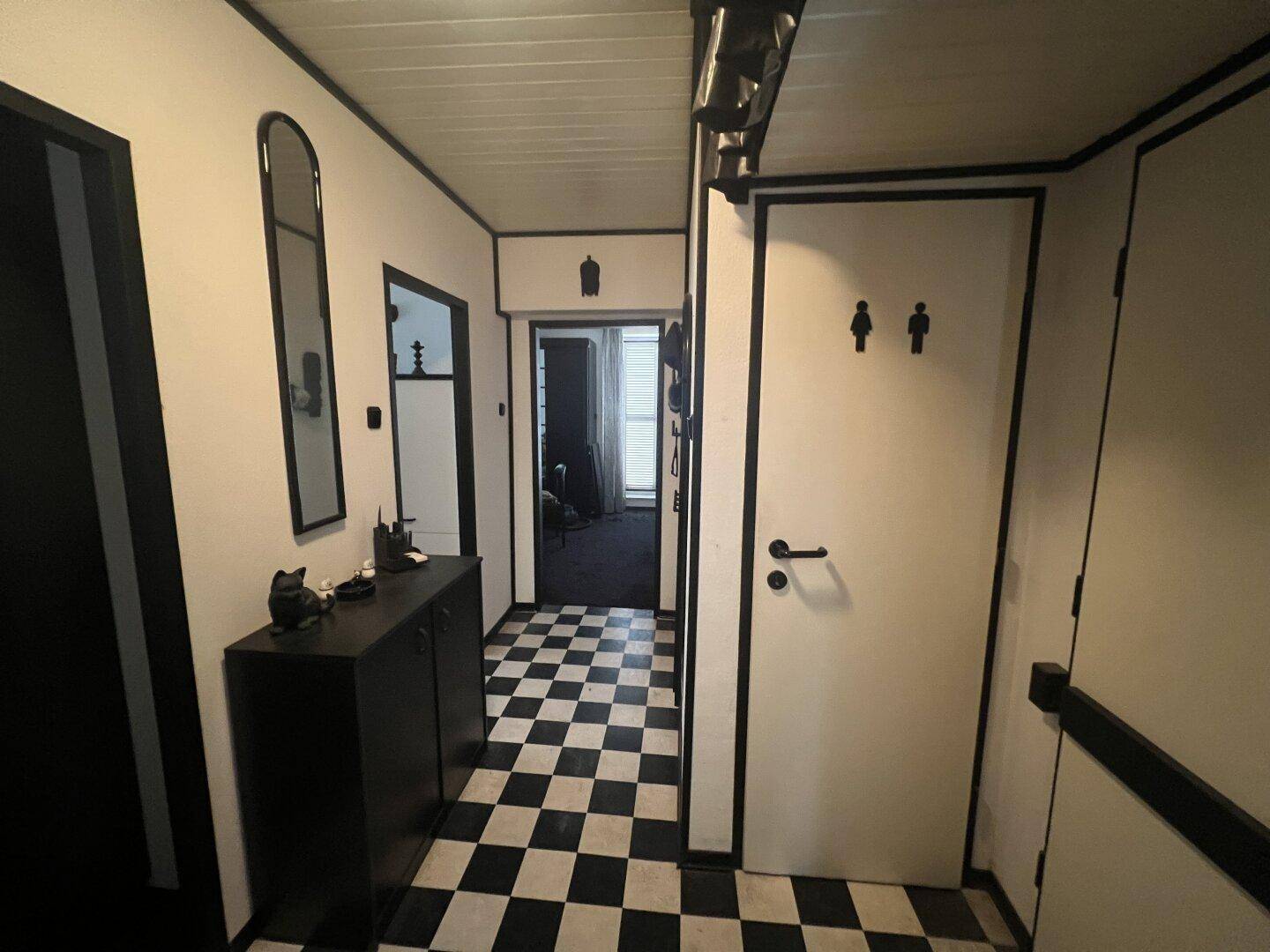 Flur mit schwarz-weiß kariertem Boden und einer Tür, die zu einem WC führt.