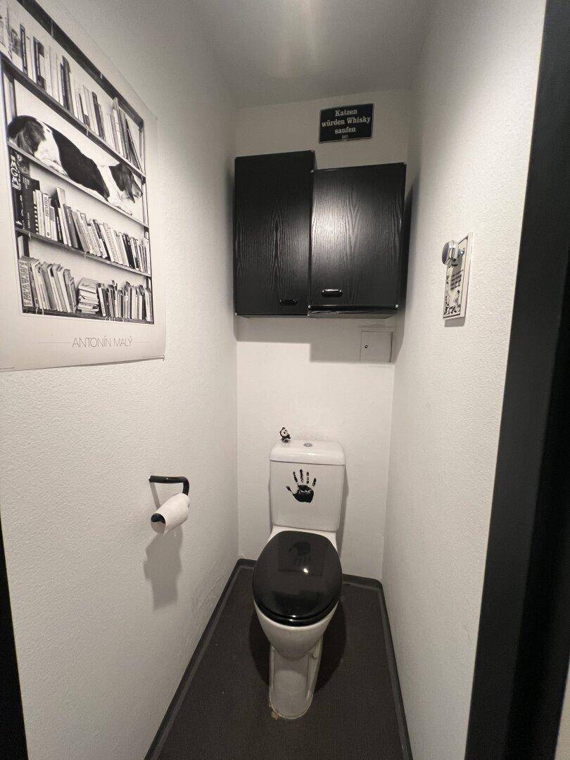 Kleines Gäste-WC mit Toilette, dunklem Boden und einem Hängeschrank.