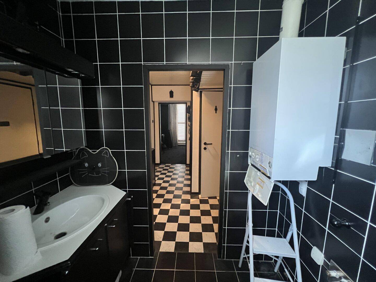 Kleines Badezimmer mit schwarzen Fliesen, Waschbecken und einem Warmwasserboiler.