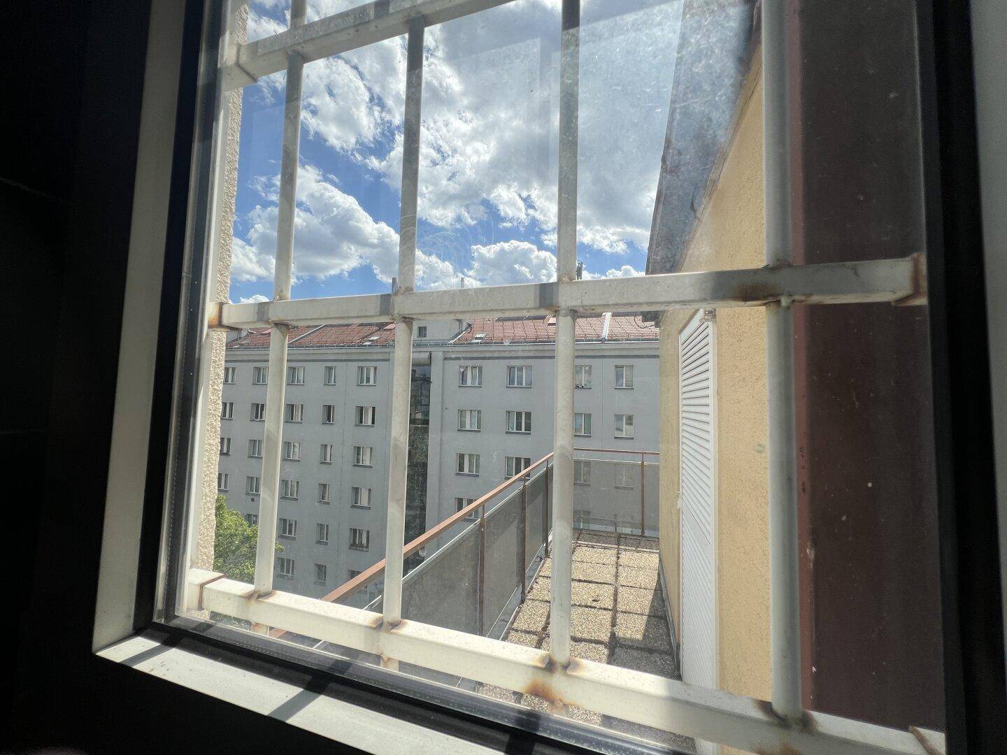 Blick aus einem Fenster mit Gitterstäben auf andere Gebäude und den blauen Himmel.