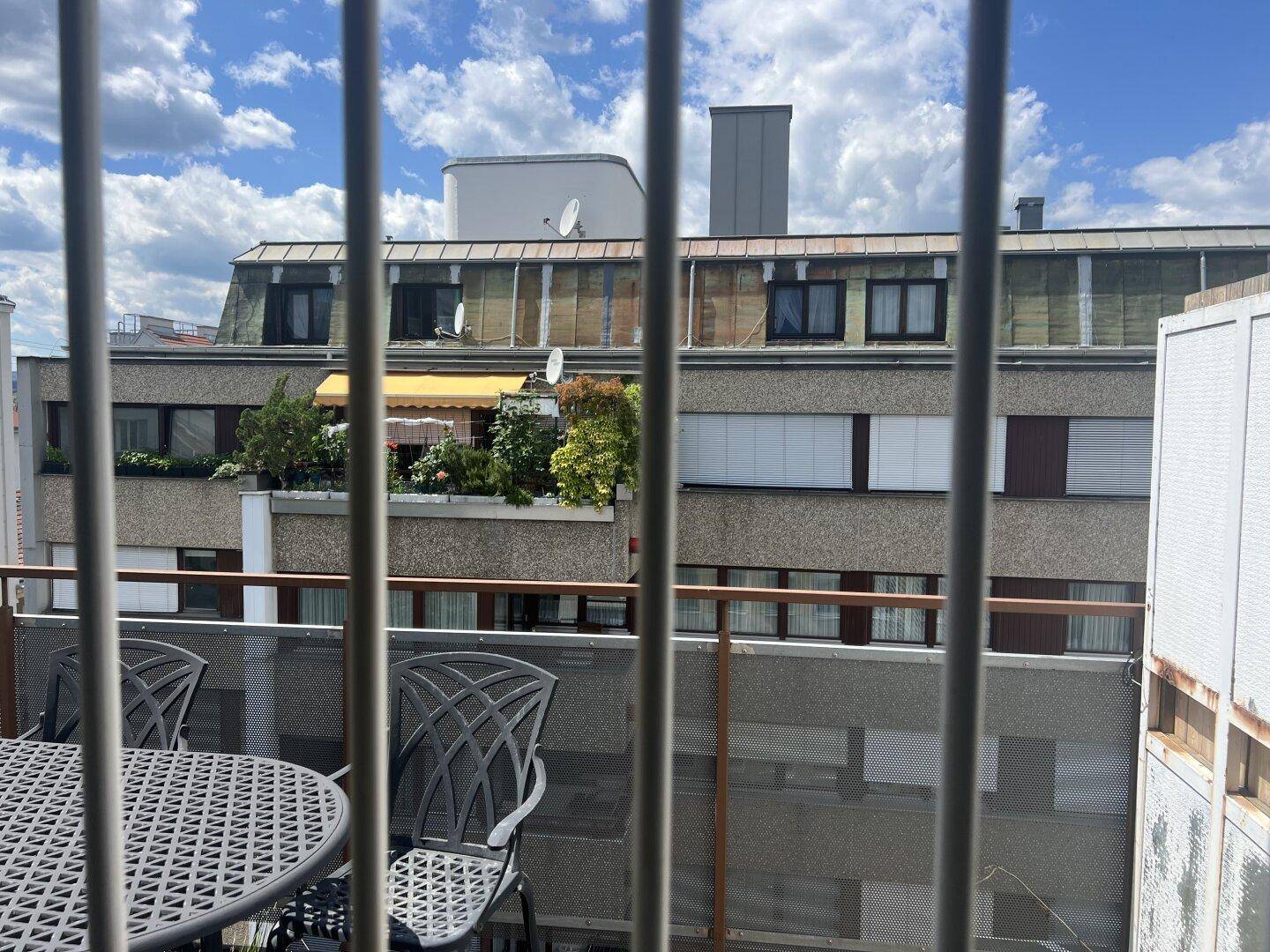 Blick von einem Balkon mit Gartenmöbeln auf die umliegenden Gebäude und den Himmel.