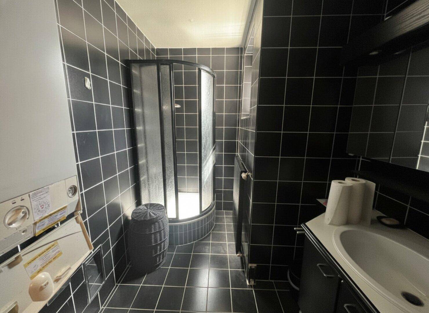 Badezimmer mit schwarzen Fliesen, einer Eckdusche und einem Waschbeckenunterschrank.
